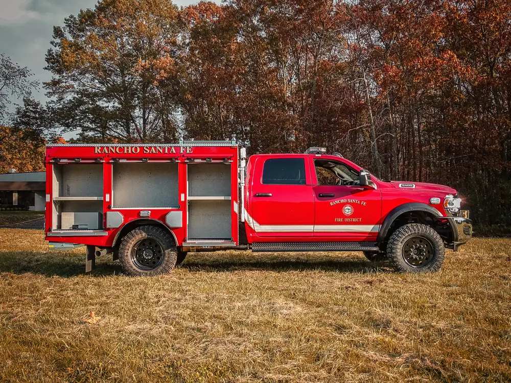 Exterior view of small fire truck showing cab, body compartments, and wheel/tire area.