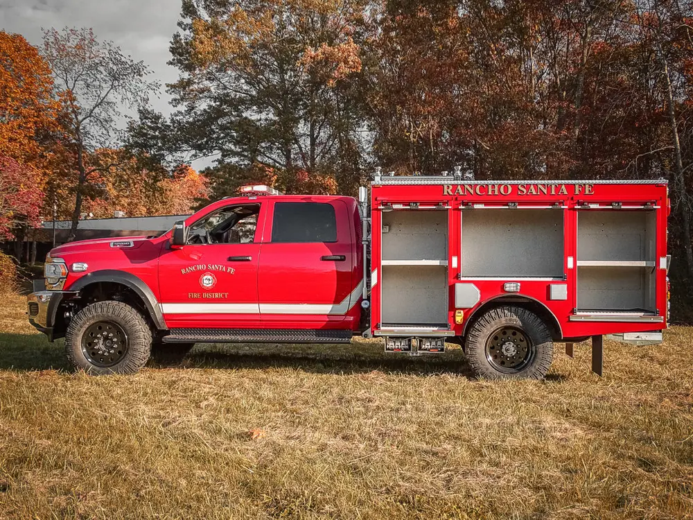 Exterior view of small fire truck showing cab, body compartments, and wheel/tire area.
