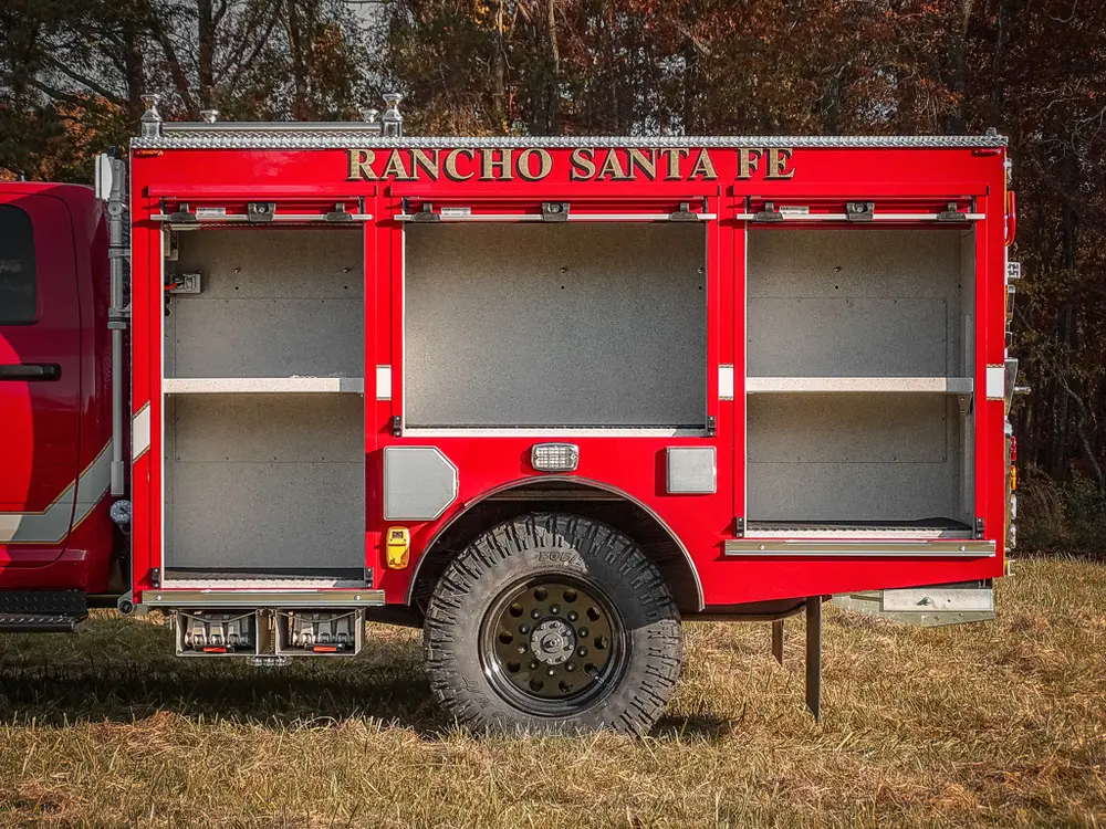 Exterior view of small fire truck showing cab, body compartments, and wheel/tire area.
