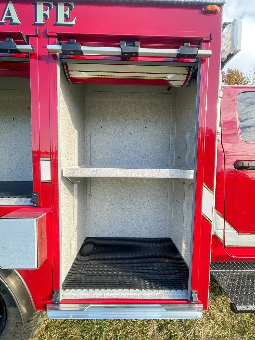 Exterior view of small fire truck showing cab, body compartments, and wheel/tire area.