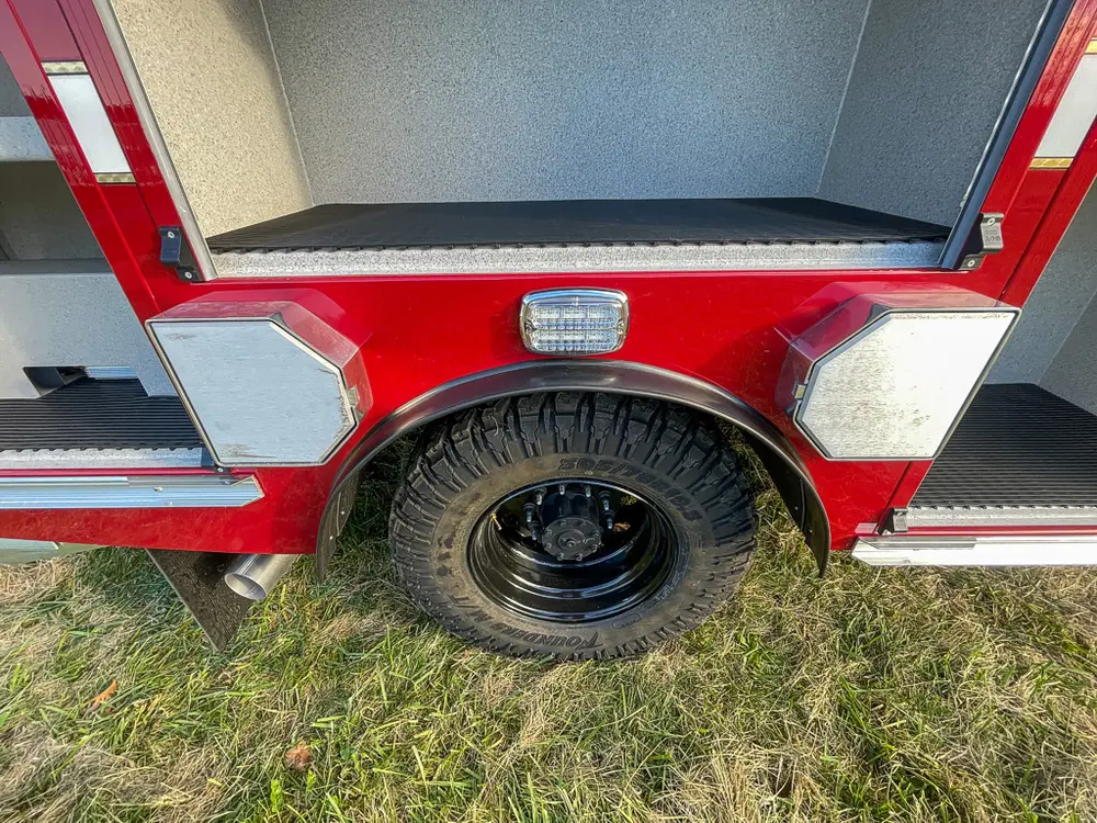Exterior view of small fire truck showing cab, body compartments, and wheel/tire area.