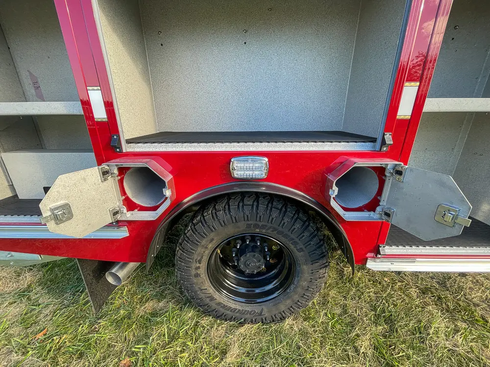 Exterior view of small fire truck showing cab, body compartments, and wheel/tire area.