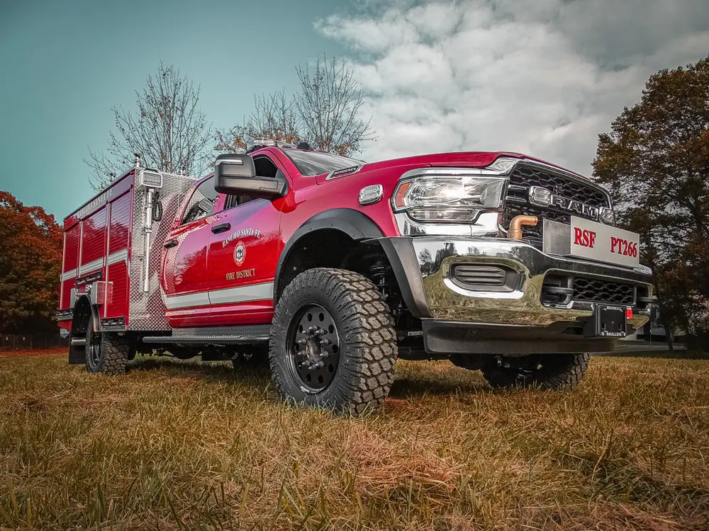 Exterior view of small fire truck showing cab, body compartments, and wheel/tire area.