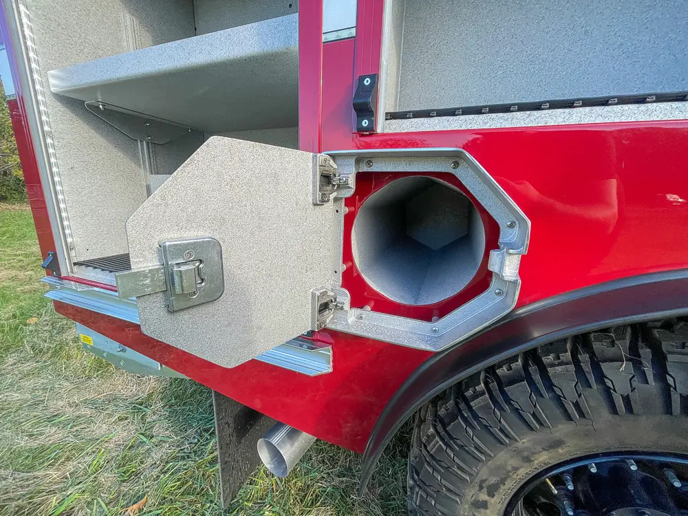 Exterior view of small fire truck showing cab, body compartments, and wheel/tire area.