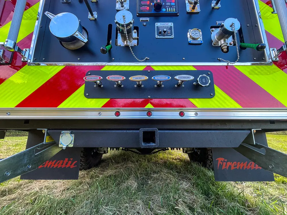 Exterior view of small fire truck showing cab, body compartments, and wheel/tire area.