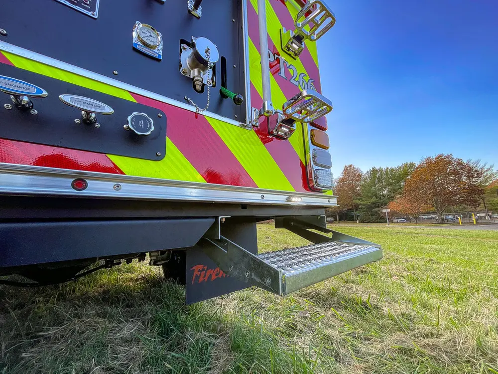 Exterior view of small fire truck showing cab, body compartments, and wheel/tire area.