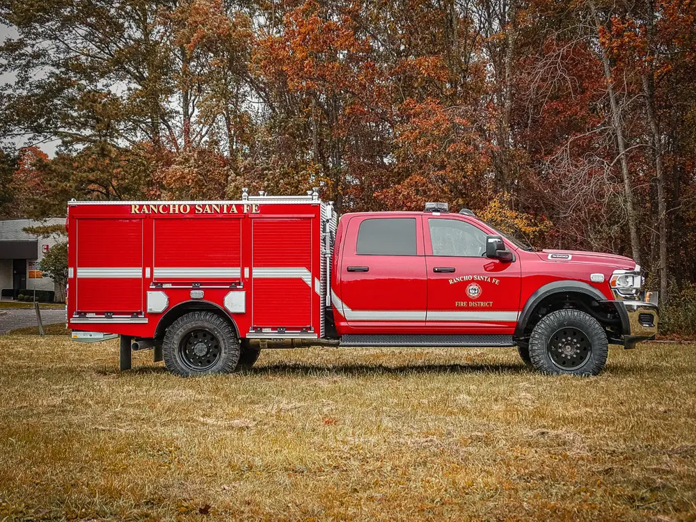 Exterior view of small fire truck showing cab, body compartments, and wheel/tire area.