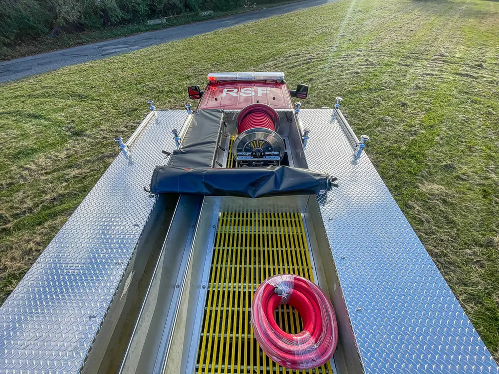 Exterior view of small fire truck showing cab, body compartments, and wheel/tire area.