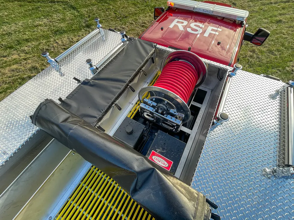 Exterior view of small fire truck showing cab, body compartments, and wheel/tire area.