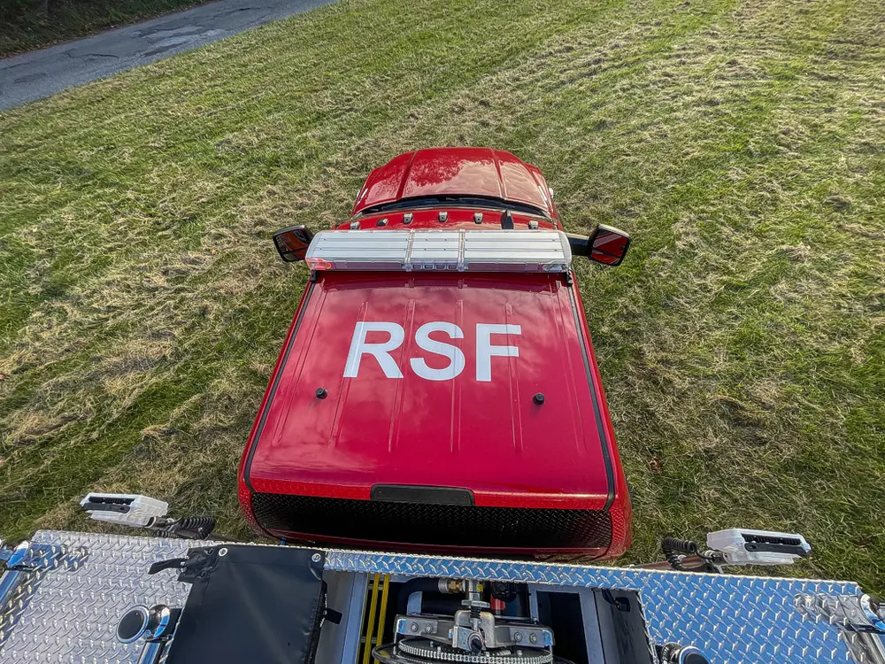 Exterior view of small fire truck showing cab, body compartments, and wheel/tire area.