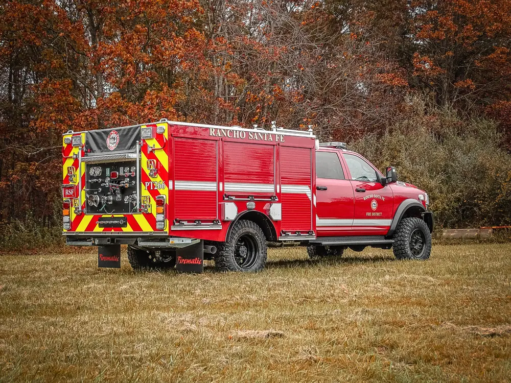 Exterior view of small fire truck showing cab, body compartments, and wheel/tire area.