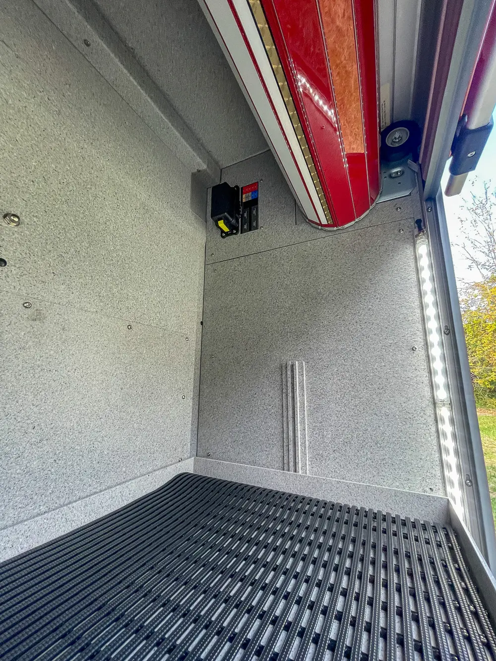 Exterior view of small fire truck showing cab, body compartments, and wheel/tire area.