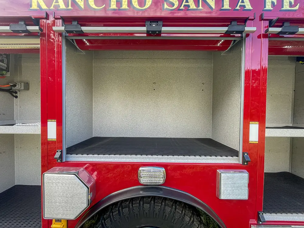 Exterior view of small fire truck showing cab, body compartments, and wheel/tire area.