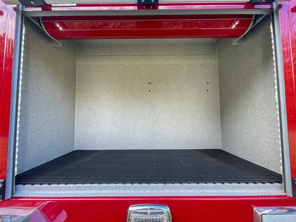 Exterior view of small fire truck showing cab, body compartments, and wheel/tire area.