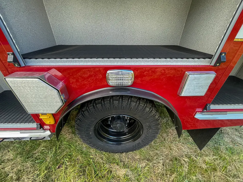 Exterior view of small fire truck showing cab, body compartments, and wheel/tire area.