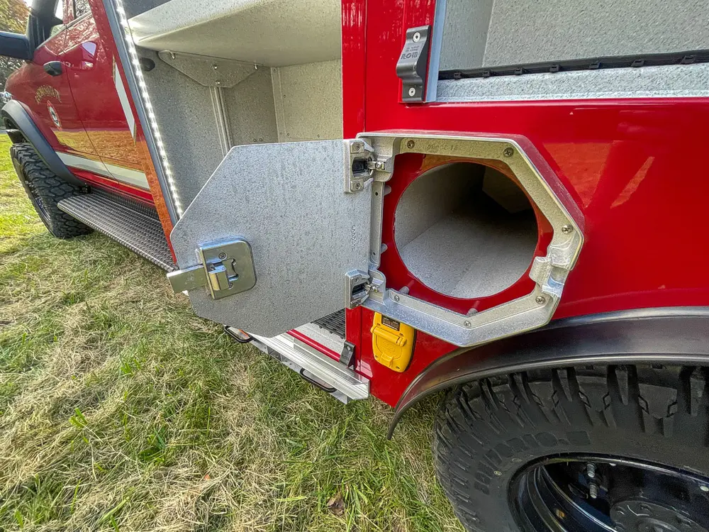 Exterior view of small fire truck showing cab, body compartments, and wheel/tire area.