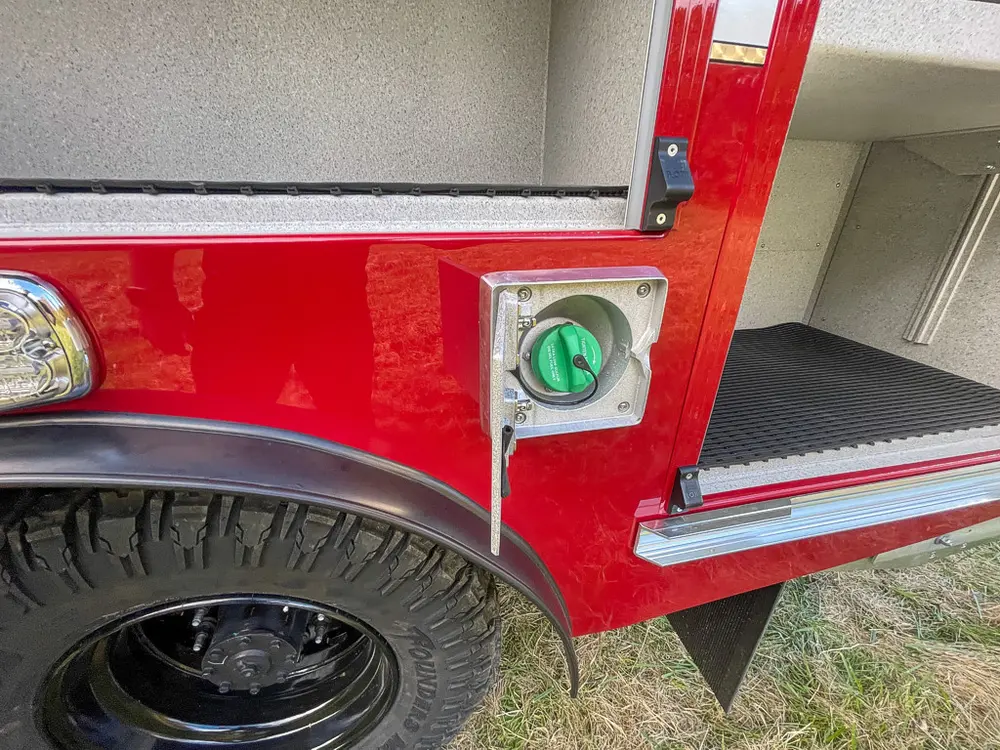 Exterior view of small fire truck showing cab, body compartments, and wheel/tire area.