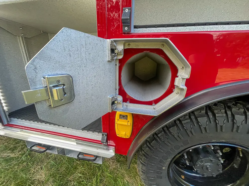 Exterior view of small fire truck showing cab, body compartments, and wheel/tire area.