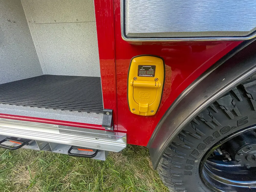 Exterior view of small fire truck showing cab, body compartments, and wheel/tire area.