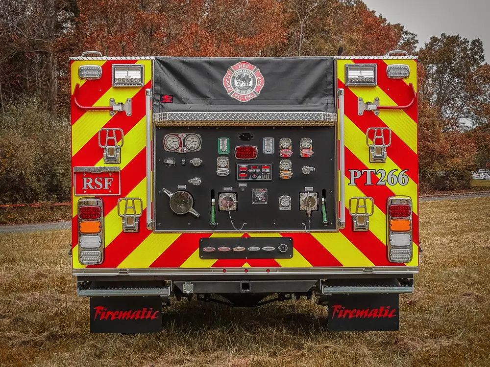 Exterior view of small fire truck showing cab, body compartments, and wheel/tire area.