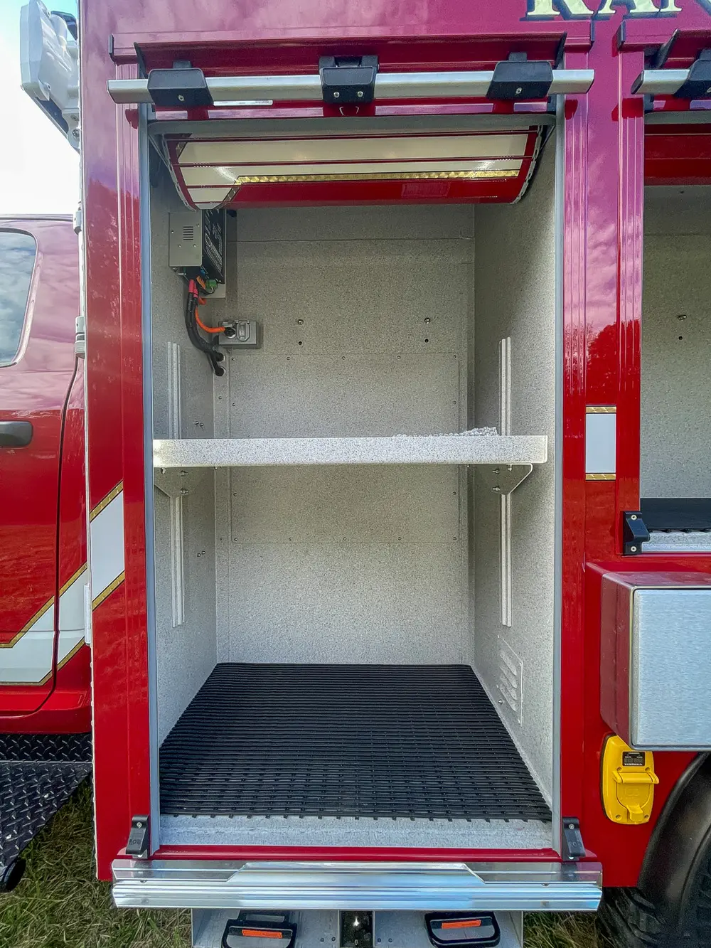 Exterior view of small fire truck showing cab, body compartments, and wheel/tire area.