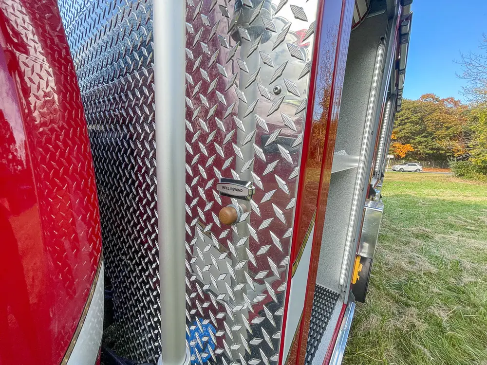 Exterior view of small fire truck showing cab, body compartments, and wheel/tire area.