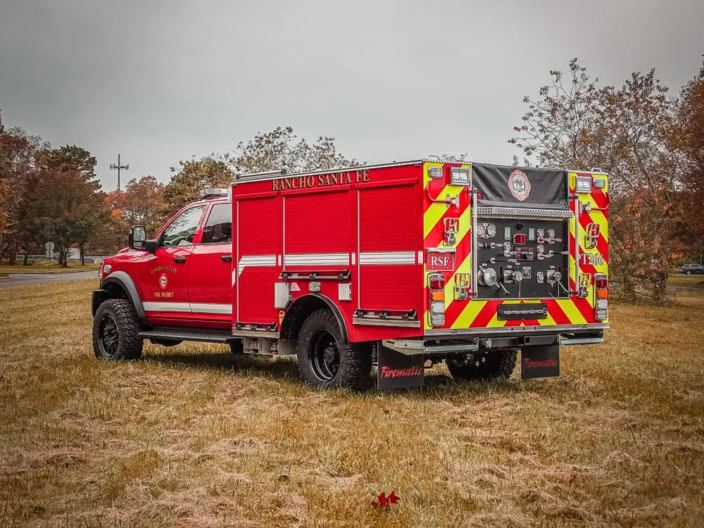 Exterior view of small fire truck showing cab, body compartments, and wheel/tire area.