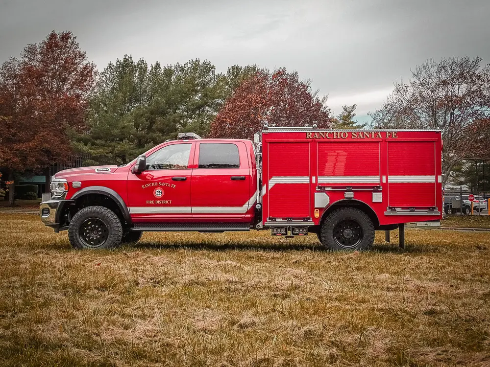 Exterior view of small fire truck showing cab, body compartments, and wheel/tire area.