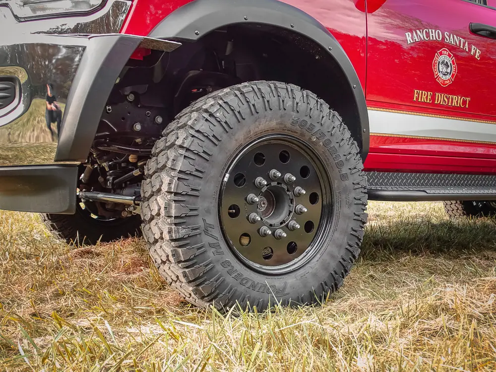 Exterior view of small fire truck showing cab, body compartments, and wheel/tire area.