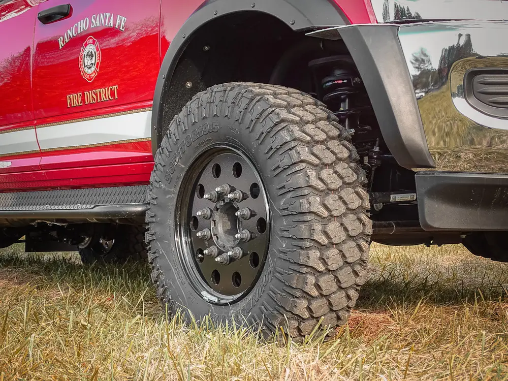 Exterior view of small fire truck showing cab, body compartments, and wheel/tire area.