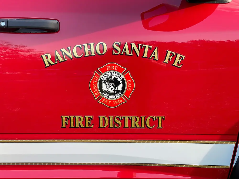 Exterior view of small fire truck showing cab, body compartments, and wheel/tire area.