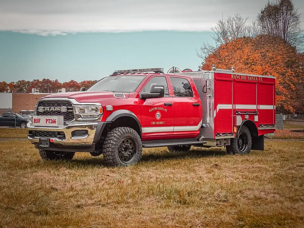 Exterior view of small fire truck showing cab, body compartments, and wheel/tire area.