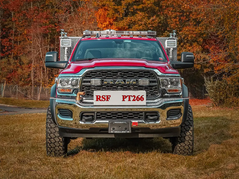 Exterior view of small fire truck showing cab, body compartments, and wheel/tire area.