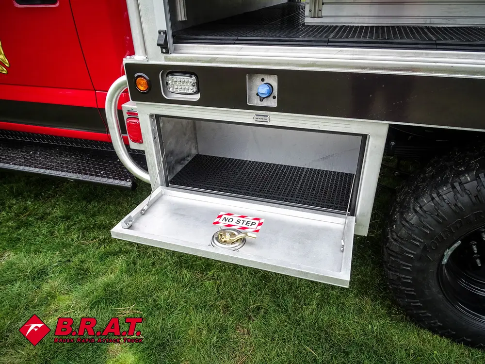Exterior view of small fire truck showing cab, body compartments, and wheel/tire area.