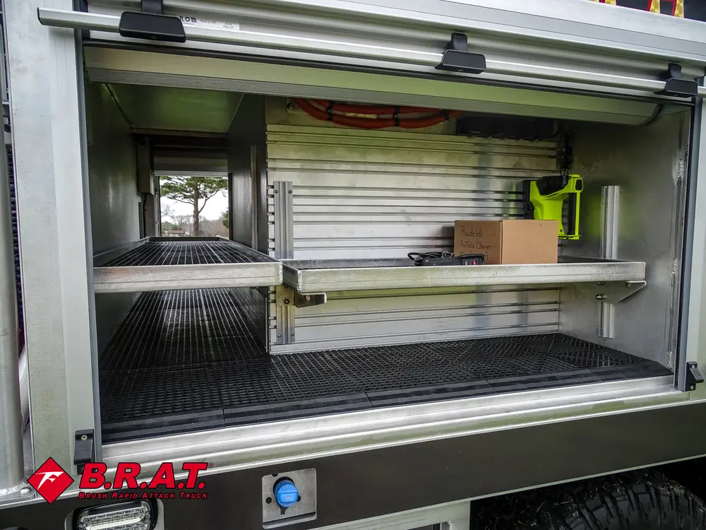 Exterior view of small fire truck showing cab, body compartments, and wheel/tire area.