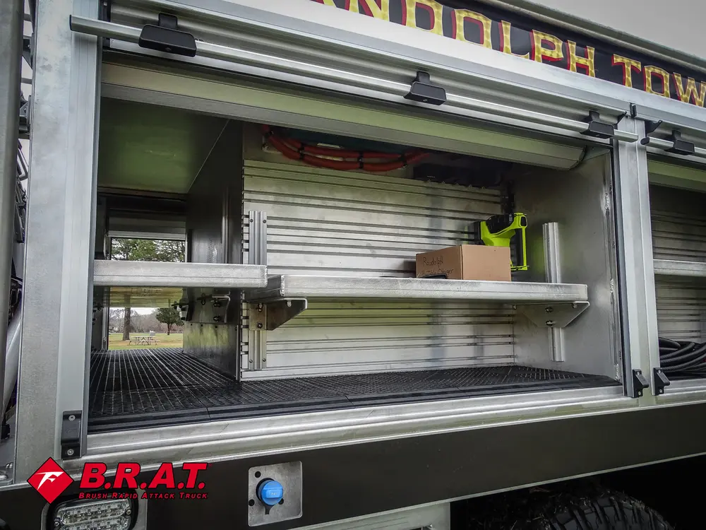 Exterior view of small fire truck showing cab, body compartments, and wheel/tire area.