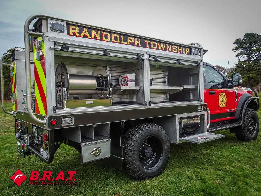 Exterior view of small fire truck showing cab, body compartments, and wheel/tire area.