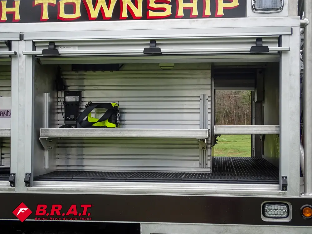 Exterior view of small fire truck showing cab, body compartments, and wheel/tire area.