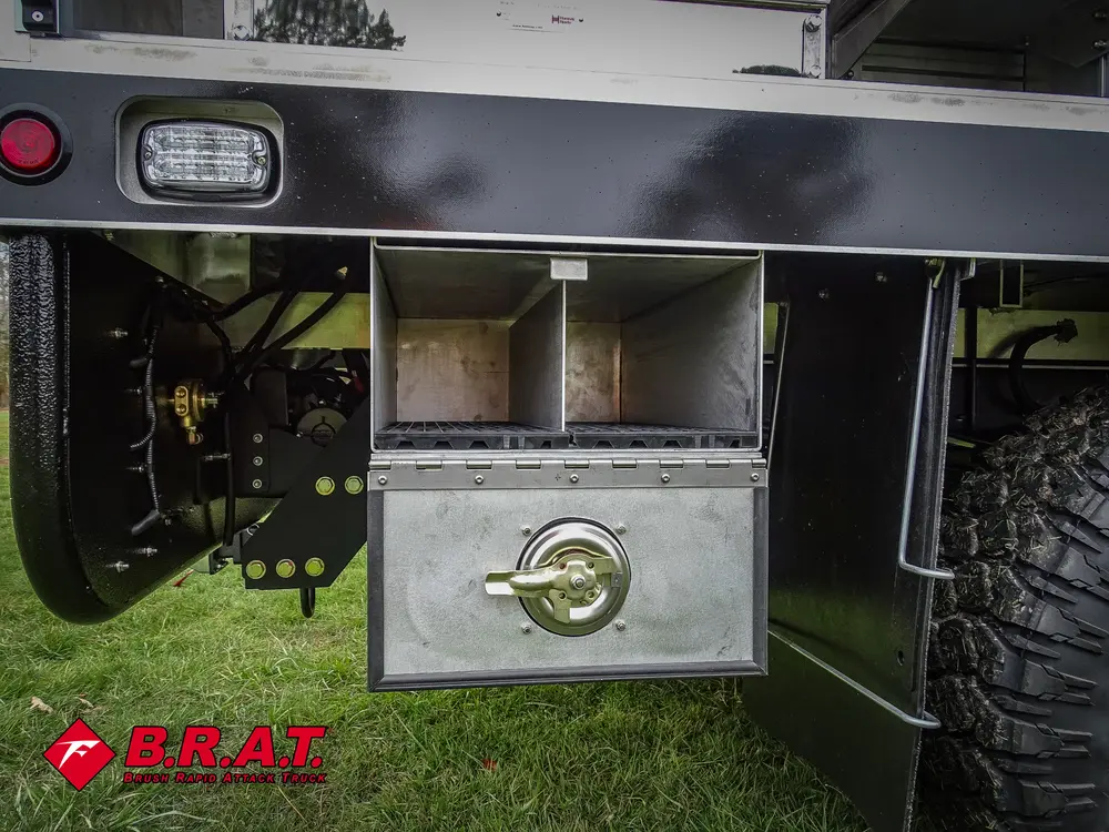 Exterior view of small fire truck showing cab, body compartments, and wheel/tire area.