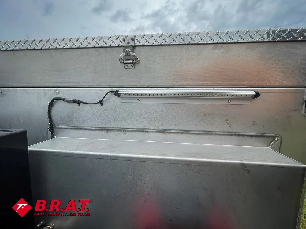 Exterior view of small fire truck showing cab, body compartments, and wheel/tire area.