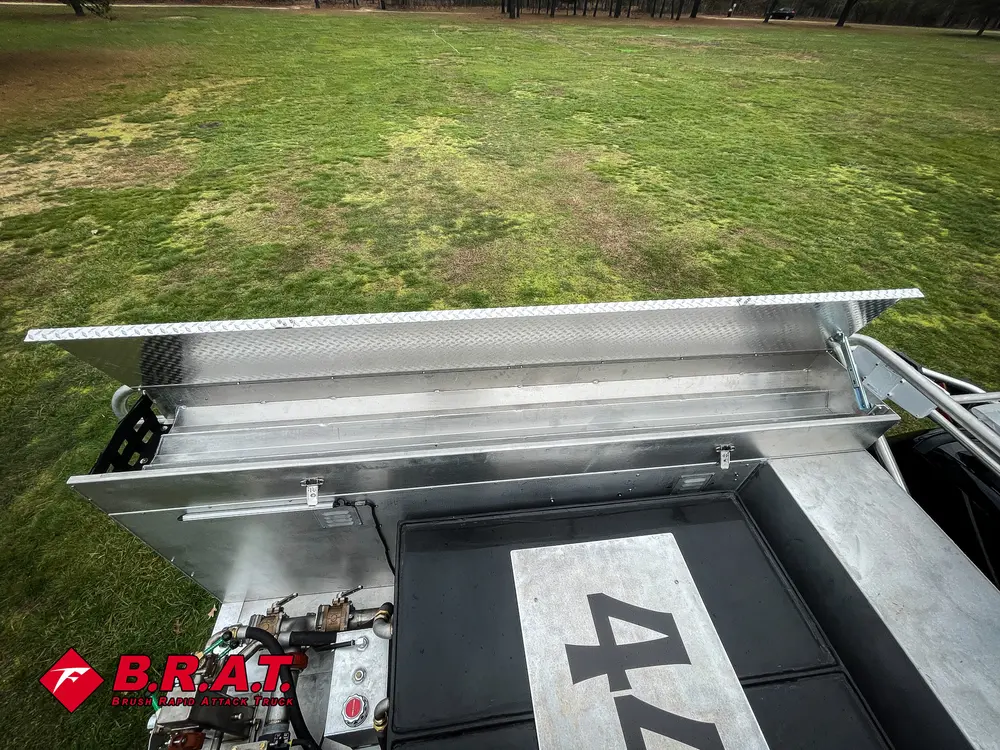 Exterior view of small fire truck showing cab, body compartments, and wheel/tire area.