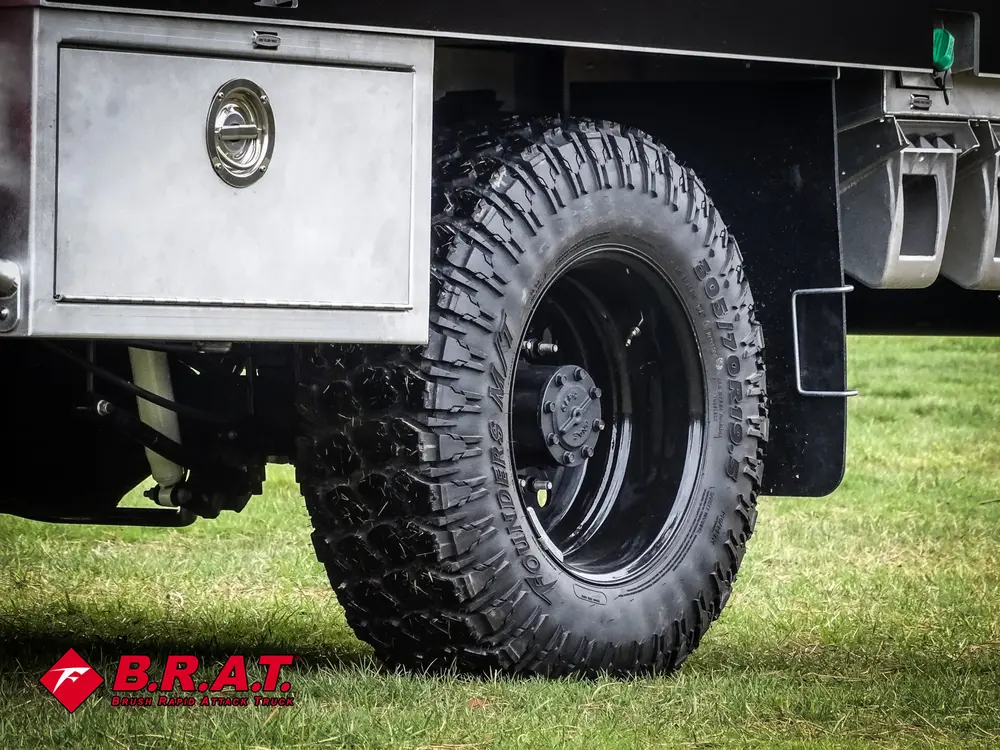 Exterior view of small fire truck showing cab, body compartments, and wheel/tire area.