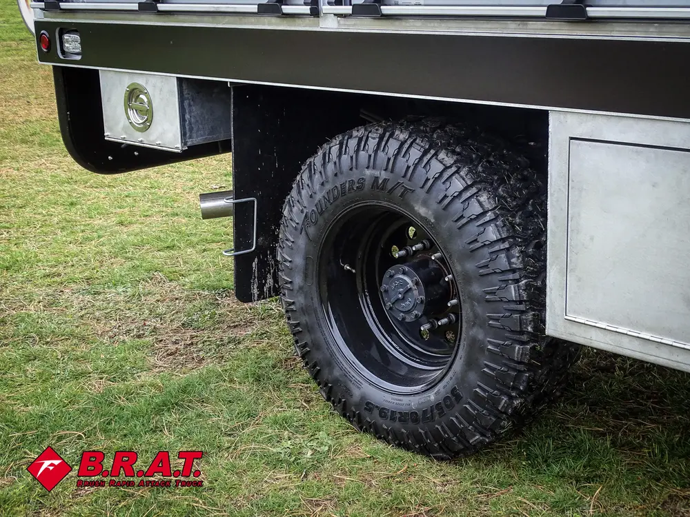 Exterior view of small fire truck showing cab, body compartments, and wheel/tire area.