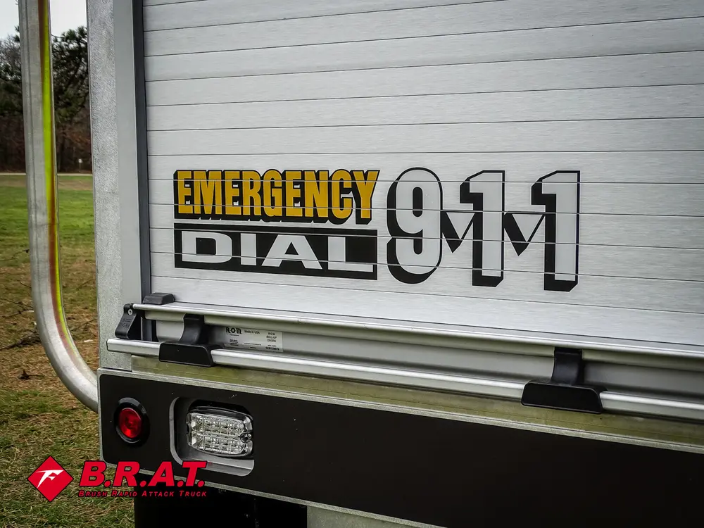 Exterior view of small fire truck showing cab, body compartments, and wheel/tire area.