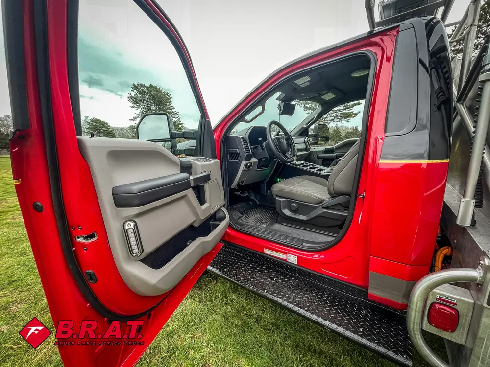 Exterior view of small fire truck showing cab, body compartments, and wheel/tire area.