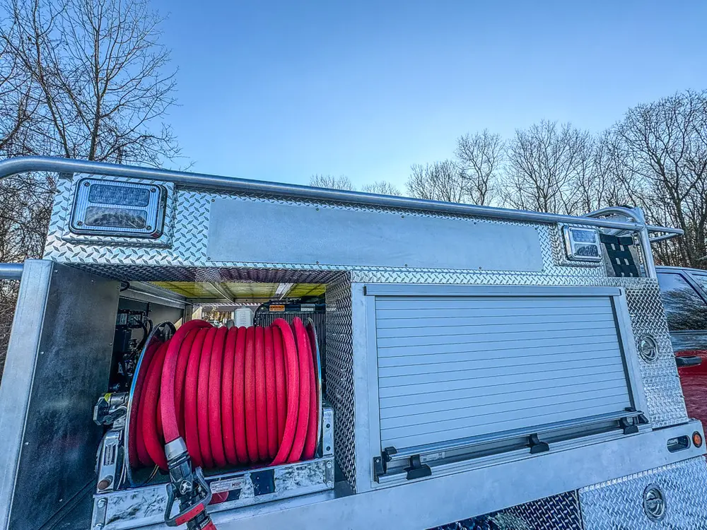 Side compartment view with red hose reel and closed roll-up panel beside it.