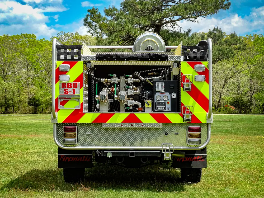 Exterior view of small fire truck showing cab, body compartments, and wheel/tire area.