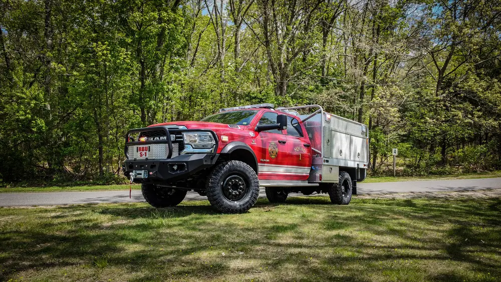 Exterior view of small fire truck showing cab, body compartments, and wheel/tire area.