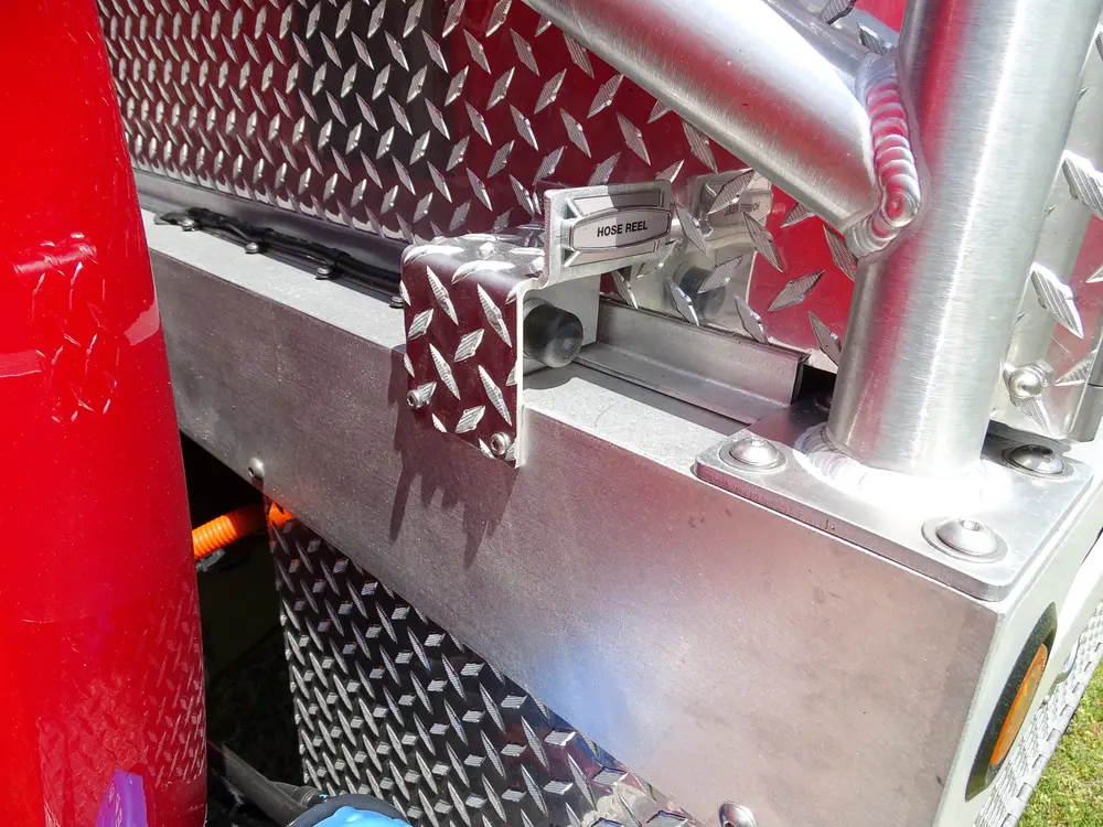 Exterior view of small fire truck showing cab, body compartments, and wheel/tire area.