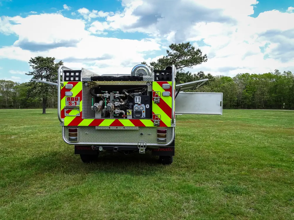 Exterior view of small fire truck showing cab, body compartments, and wheel/tire area.